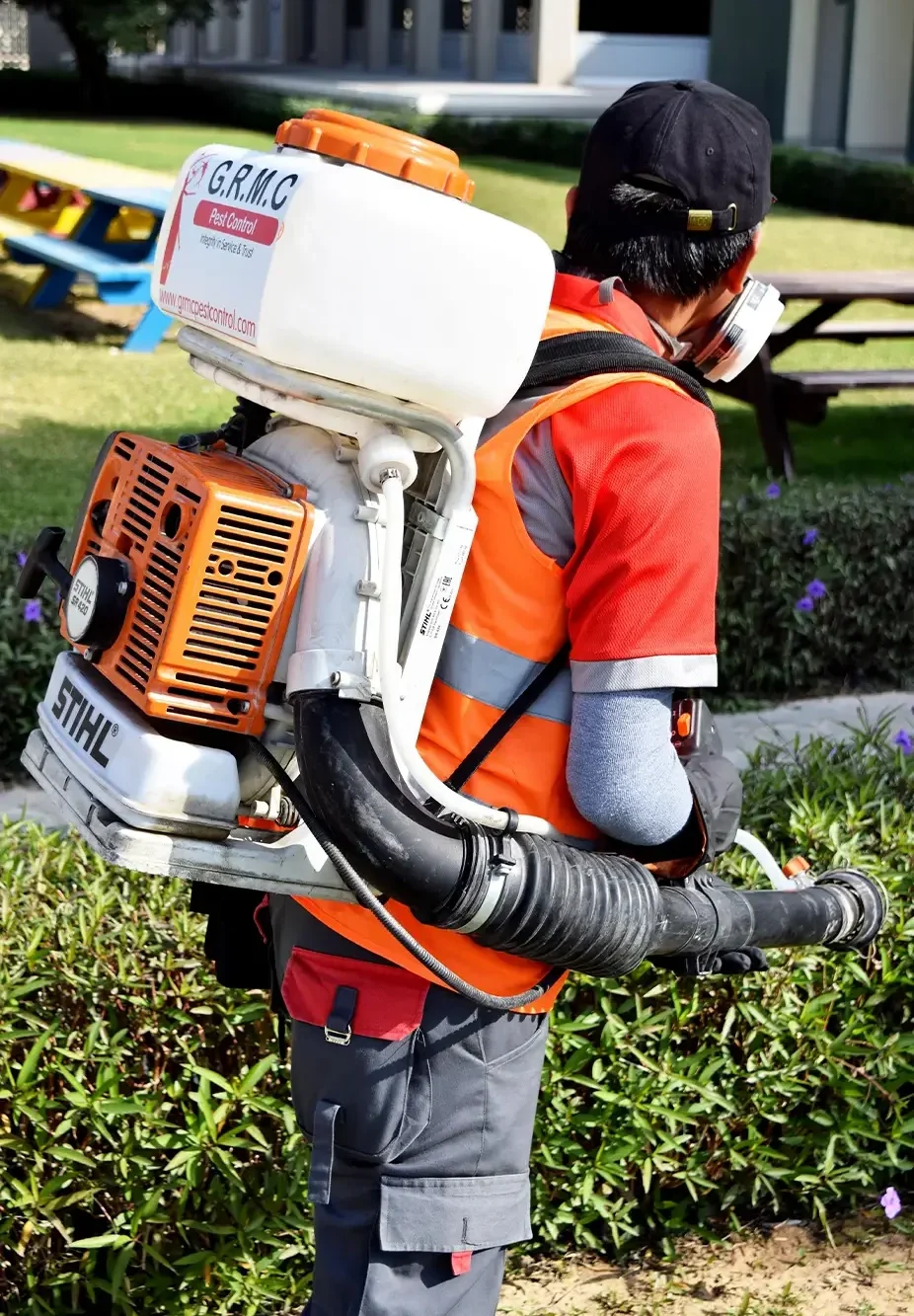 GRMC pest control professional in uniform spraying non-toxic, eco-friendly pesticides outside.